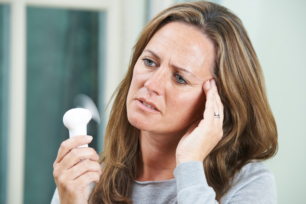 A woman going through menopause holding a personal fan
